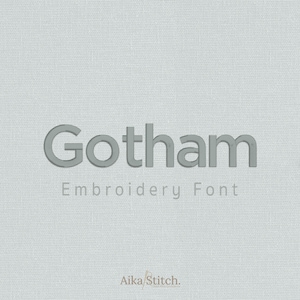 May include: A light gray fabric background featuring the dark gray text Gotham Embroidery Font in a bold sans-serif typeface, with the smaller text Aika Stitch centered at the bottom in a thin, light brown font style.