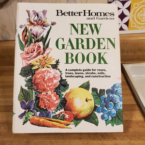 May include: A white book titled "Better Homes and Gardens New Garden Book" with a colorful illustration of flowers, fruits, and vegetables. The book is a complete guide for roses, trees, lawns, shrubs, soils, landscaping, and construction.