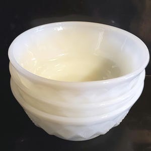 May include: A white, opaque glass bowl with a layered, textured design. The bowl has a smooth, rounded interior and a decorative, geometric pattern on the exterior. The bowl is likely vintage and suitable for serving or display.