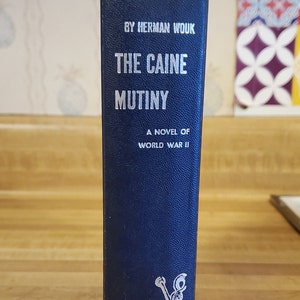 May include: A blue hardcover book titled "The Caine Mutiny" by Herman Wouk. The book is a novel of World War II and features an anchor on the cover. The book is published by Doubleday.
