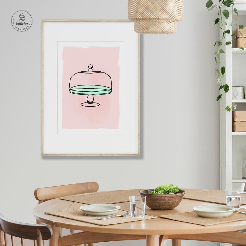 Kitchen wall art of cake stand with blue plate on pink background. Shown in kitchen.