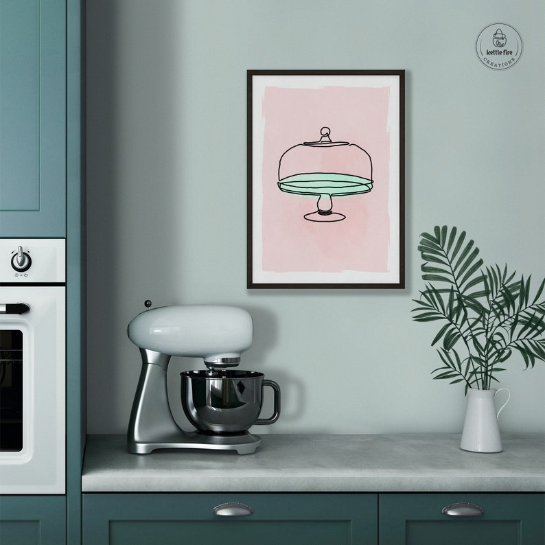 Kitchen wall art of cake stand with blue plate on pink background. Shown in kitchen.