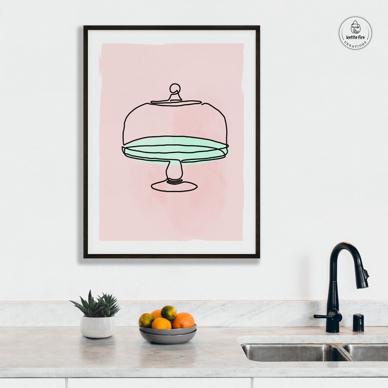 Kitchen wall art of cake stand with blue plate on pink background. Shown in kitchen.