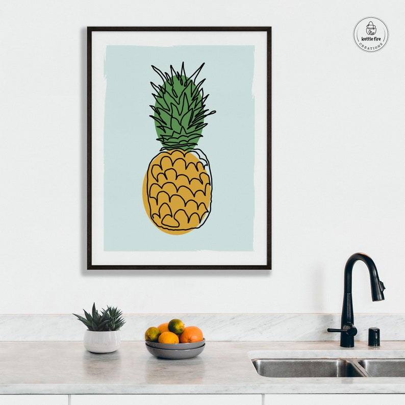 Kitchen wall art of pineapple with gold base and green leaves on blue background. Shown in kitchen.