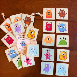 May include: A wooden memory matching game featuring square tiles with colorful monster illustrations. The set includes a drawstring bag and a card labeled Wooden Match Game Monsters Handcrafted in Houston. The tiles display various creatures.
