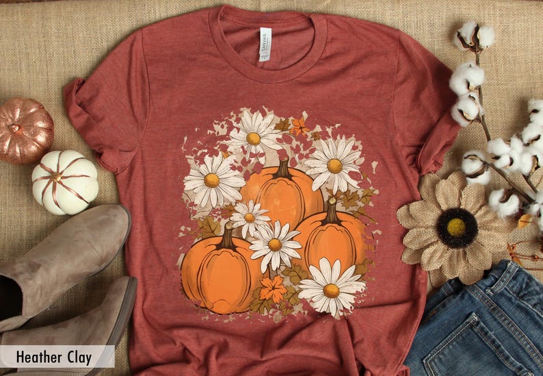 May include: A rust-colored t-shirt with a graphic print of pumpkins and white daisies. The graphic has a distressed, vintage look.