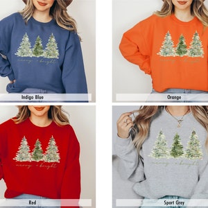 May include: A Christmas sweatshirt featuring a watercolour design of three pine trees and the text "merry & bright". The sweatshirt is available in four colours: indigo blue, orange, red, and sport grey.