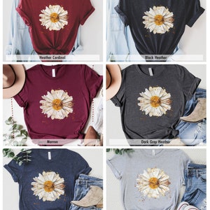 Pode incluir: Uma camiseta com uma estampa de margarida em aquarela em v&aacute;rias cores, incluindo marrom, vermelho-cardeal mesclado, preto mesclado, cinza escuro mesclado, azul marinho mesclado e cinza mesclado atl&eacute;tico.