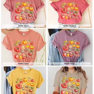May include: Six different colored t-shirts with a graphic print of a variety of tomatoes, including red, yellow, and green tomatoes. The t-shirts are available in Heather Mauve, Heather Raspberry, Heather Sunset, Heather Orchid, Heather Yellow Gold, and Heather Tan.