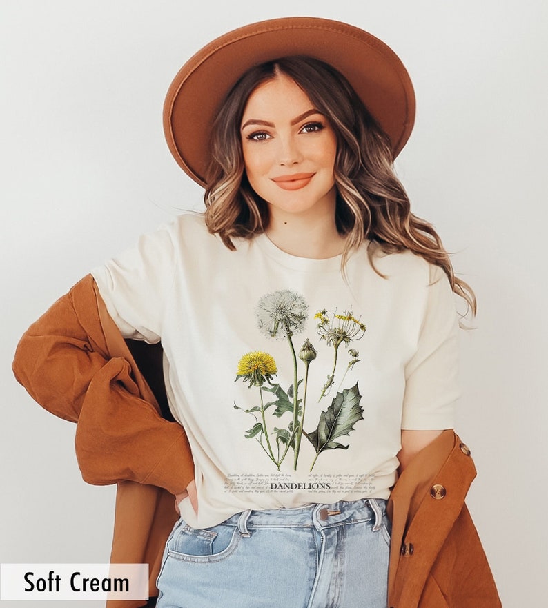 May include: A soft cream colored t-shirt with a botanical illustration of dandelions. The text "DANDELIONS" is printed below the illustration.