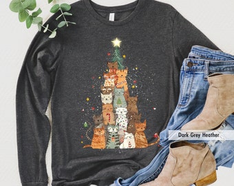 May include: A dark gray heather long-sleeve shirt with a Christmas tree design featuring a stack of cats. The cats are all different colors and have different expressions. The tree is decorated with lights, ornaments, and a star on top. The text "Dark Grey Heather" is visible in the bottom right corner of the image.