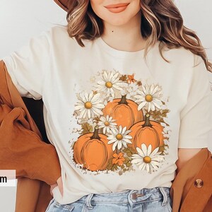 May include: A soft cream t-shirt with a graphic print of orange pumpkins and white daisies. The graphic is centered on the shirt.