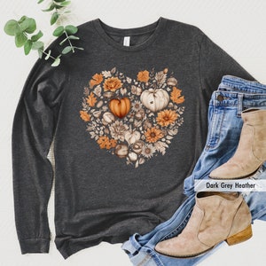 May include: A long-sleeved, dark gray heather t-shirt with a heart-shaped design featuring fall-themed illustrations of pumpkins, leaves, and acorns. The text "Dark Grey Heather" is visible in the bottom right corner of the image.
