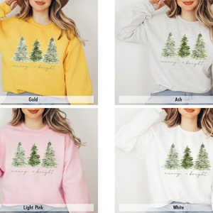 May include: A sweatshirt featuring a watercolour design of three Christmas trees and the text "merry & bright" in gold lettering. The sweatshirt is available in four colours: gold, ash, light pink, and white.