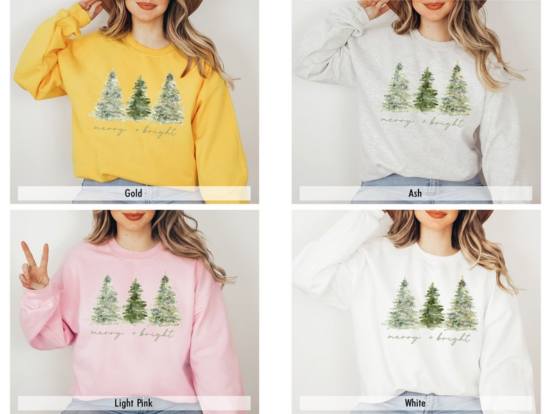 May include: A sweatshirt featuring a watercolour design of three Christmas trees and the text "merry & bright" in gold lettering. The sweatshirt is available in four colours: gold, ash, light pink, and white.