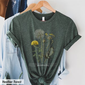 May include: A green heather forest t-shirt with a botanical illustration of dandelions in shades of yellow, white, and green. The text "DANDELIONS" is printed in white below the illustration.