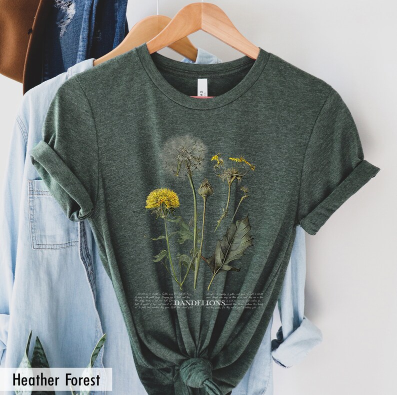 May include: A green heather forest t-shirt with a botanical illustration of dandelions in shades of yellow, white, and green. The text "DANDELIONS" is printed in white below the illustration.