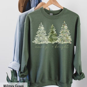May include: A green sweatshirt featuring a watercolour design of three Christmas trees and the text "merry + bright".
