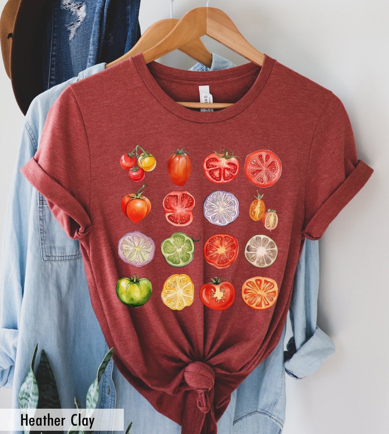 May include: A maroon t-shirt with a graphic print of various red, green, yellow, and purple fruits and vegetables. The fruits and vegetables are arranged in a grid pattern and include tomatoes, limes, lemons, and bell peppers.