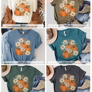 May include: Six different color t-shirts with a graphic print of pumpkins and daisies. The colors are natural, heather olive, heather slate, heather deep teal, heather forest, and dark grey heather.