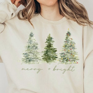 May include: A beige sweatshirt with a Christmas tree design and the text "merry + bright" printed on the front.