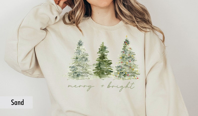 May include: A beige sweatshirt with a Christmas tree design and the text "merry + bright" printed on the front.