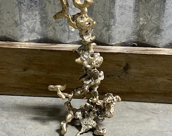 May include: A gold-colored metal sculpture resembling a termite mound. The sculpture is abstract and organic in shape, with a textured surface.