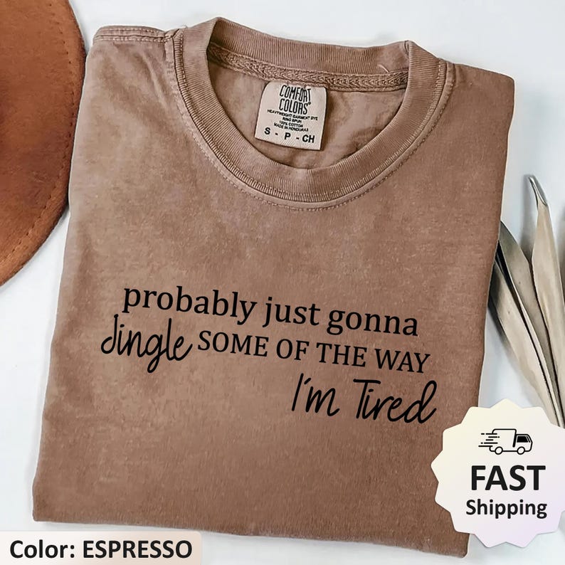 May include: Espresso-colored Comfort Colors t-shirt with the text "probably just gonna jingle some of the way I'm Tired" in black. The shirt has a crew neck and short sleeves. The tag reads "Comfort Colors".