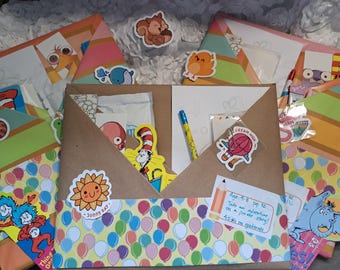 May include: A collection of colorful Dr. Seuss-themed stationery and stickers. The image features a brown paper envelope with a balloon pattern, a yellow pen, and various stickers, including a sun, squirrel, and characters from the books.