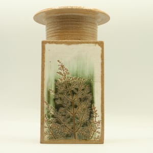 May include: A rectangular ceramic vase with a light brown top and base, and a central panel featuring a green and white background with a detailed botanical design. The vase has a textured surface.