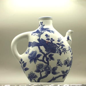 May include: White ceramic pitcher with a blue floral and bird design. The pitcher has a handle and a spout. The design includes flowers, birds, and branches. The pitcher is approximately 8 inches tall.