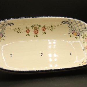 Puede incluir: Un plato de servir de cerámica blanca con diseños florales azules y morados y dos asas moradas. El plato tiene forma ovalada y un acabado brillante.