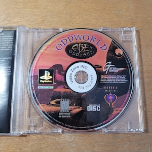 May include: A PlayStation game disc for "Oddworld: Abe's Oddysee" in a clear plastic case. The disc features a desert landscape design with the game title and PlayStation logo. The disc is labeled "Compact Disc".