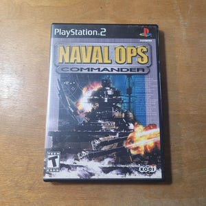Puede incluir: Caja de videojuego de PlayStation 2 para "Naval Ops: Commander". La portada presenta una ilustración detallada de una batalla naval con explosiones y barcos de guerra. El juego está clasificado como "T" para adolescentes.