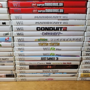 May include: A stack of video games for the Nintendo Wii console. The games include Super Mario Galaxy, Super Mario Bros. Wii, Mario Kart Wii, Conduit 2, Wii Fit Plus, Just Dance 3, Cars Toon Mater's Tall Tales, Mummy, Broken Sword, and Crash of the Titans.