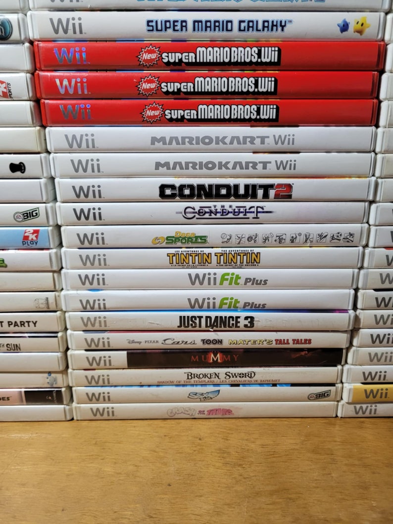 May include: A stack of video games for the Nintendo Wii console. The games include Super Mario Galaxy, Super Mario Bros. Wii, Mario Kart Wii, Conduit 2, Wii Fit Plus, Just Dance 3, Cars Toon Mater's Tall Tales, Mummy, Broken Sword, and Crash of the Titans.