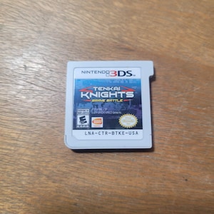 Peut inclure: Une cartouche de jeu Nintendo 3DS pour "Tenkai Knights: Brave Battle". La cartouche de jeu est blanche avec une étiquette bleue et rouge. L'étiquette présente le titre du jeu et le logo Nintendo 3DS.
