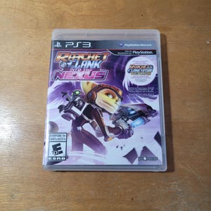 May include: A video game case for the PlayStation 3 console featuring Ratchet & Clank: Into the Nexus. The case is purple and black with a picture of Ratchet and Clank on the front. The game is rated E for Everyone 10+ by the ESRB.