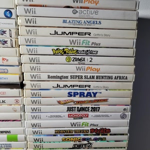 May include: A stack of 20 video game cartridges for the Nintendo Wii console. The games include titles like "Wii Play", "Blazing Angels", "Jumper", "Wii Fit Plus", "Raving Rabbids Travel in Time", "Zumba 2", "Remington Super Slam Hunting Africa", "Spray", "Hot Wheels Track Attack", "Just Dance 2017", "Monopoly Streets", "Monster Trucks Mayhem", "Sonic Colors", "Dirt 2", "Mathews Bowhunting", and "Wii Sports Resort".
