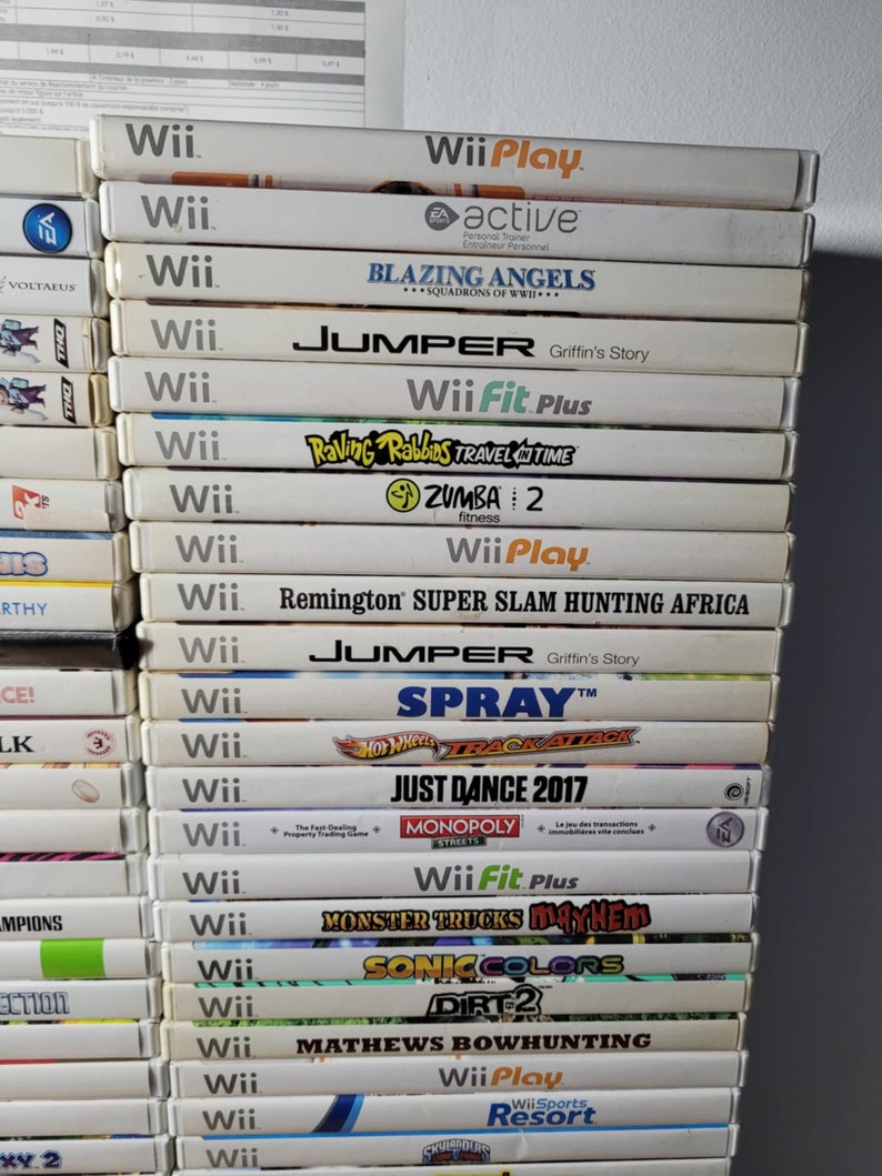 May include: A stack of 20 video game cartridges for the Nintendo Wii console. The games include titles like "Wii Play", "Blazing Angels", "Jumper", "Wii Fit Plus", "Raving Rabbids Travel in Time", "Zumba 2", "Remington Super Slam Hunting Africa", "Spray", "Hot Wheels Track Attack", "Just Dance 2017", "Monopoly Streets", "Monster Trucks Mayhem", "Sonic Colors", "Dirt 2", "Mathews Bowhunting", and "Wii Sports Resort".