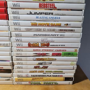 May include: A stack of 16 Nintendo Wii video game cartridges, including titles like "Redsteel", "Blazing Angels", "Bee Movie Game", "Mario Kart Wii", "Guitar Hero Warriors of Rock", "Mario Strikers Charged", "Army Men Soldiers of Misfortune", and "Tiger Woods PGA Tour 08".