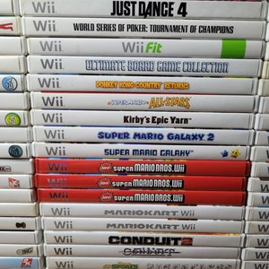 May include: A stack of video game cases for the Nintendo Wii console. The games include titles like Wario Land Shake It!, Just Dance 4, World Series of Poker: Tournament of Champions, Wii Fit, Ultimate Board Game Collection, Donkey Kong Country Returns, Super Mario All-Stars, Kirby's Epic Yarn, Super Mario Galaxy 2, Super Mario Galaxy, Super Mario Bros. Wii, Mario Kart Wii, Conduit 2, and more.