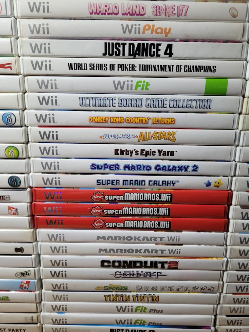 May include: A stack of video game cases for the Nintendo Wii console. The games include titles like Wario Land Shake It!, Just Dance 4, World Series of Poker: Tournament of Champions, Wii Fit, Ultimate Board Game Collection, Donkey Kong Country Returns, Super Mario All-Stars, Kirby's Epic Yarn, Super Mario Galaxy 2, Super Mario Galaxy, Super Mario Bros. Wii, Mario Kart Wii, Conduit 2, and more.