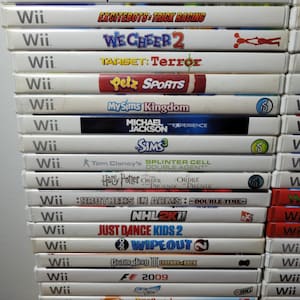 May include: A stack of 20 Nintendo Wii video game cartridges. The games include titles like Need for Speed, The Grim Adventures of Billy & Mandy, Excitebots: Trick Racing, We Cheer 2, Target: Terror, Petz Sports, MySims Kingdom, Michael Jackson: The Experience, The Sims 3, Splinter Cell: Double Agent, Harry Potter and the Order of the Phoenix, Brothers in Arms: Double Time, NHL 2K11, Just Dance Kids 2, Wipeout, Guitar Hero III: Legends of Rock, F1 2009, Dora's Crystal Kingdom, Planet 51: The Game, Where's Waldo? The Fantastic Journey, and Real Heroes: Firefighter.