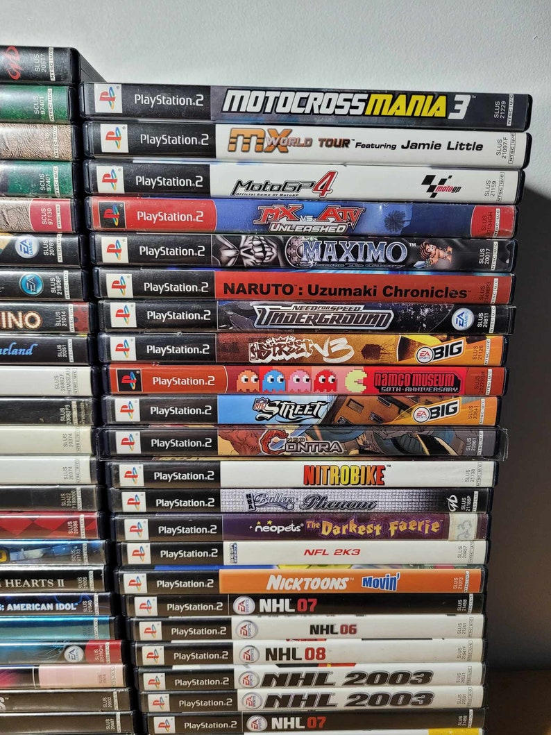 May include: A stack of PlayStation 2 video game cases, including titles like Motocross Mania 3, MX World Tour, Need for Speed Underground, and NHL 2003.