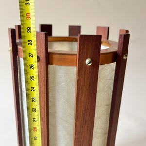 May include: A vintage wooden lamp with a cylindrical shape. The lamp is approximately 30 inches tall, featuring vertical wooden slats and a paper-like shade. The top and bottom are framed with wood, and the lamp has a warm, inviting aesthetic.