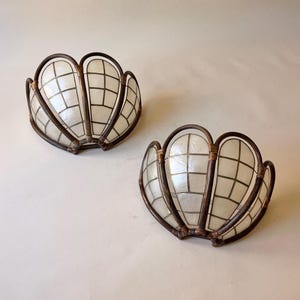 Könnte beinhalten: Zwei dekorative Schalen in Muschelform. Jede Schale hat ein weißes, gitterförmiges Innere und einen dunkelbraunen, gebogenen Metallrahmen. Die Schalen sind so gestaltet, dass sie einer Muschel ähneln.