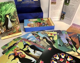 May include: A blue box with a deck of penguin tarot cards. The cards feature colorful illustrations of penguins and other animals. The box has the title "A Uulgan and Whimsical Tarot Deck" and the author's name "Dawn Evans Realtroto".