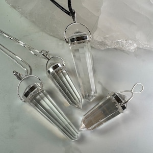 May include: Four clear quartz crystal point pendants with silver settings. The pendants are hanging from silver chains.