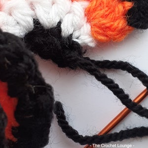 May include: Close-up of a crochet project in progress, featuring white, orange, and black yarn. The image highlights the textured stitches and the use of a crochet hook. The color palette is vibrant, showcasing the craft's detail.